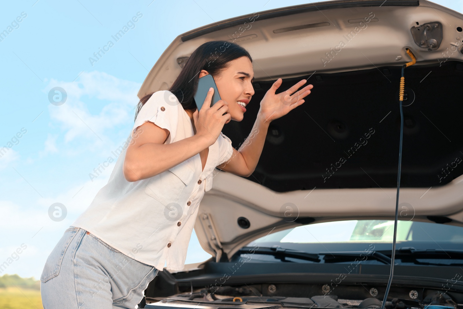 Photo of Stressed young woman talking on phone near broken car on roadside