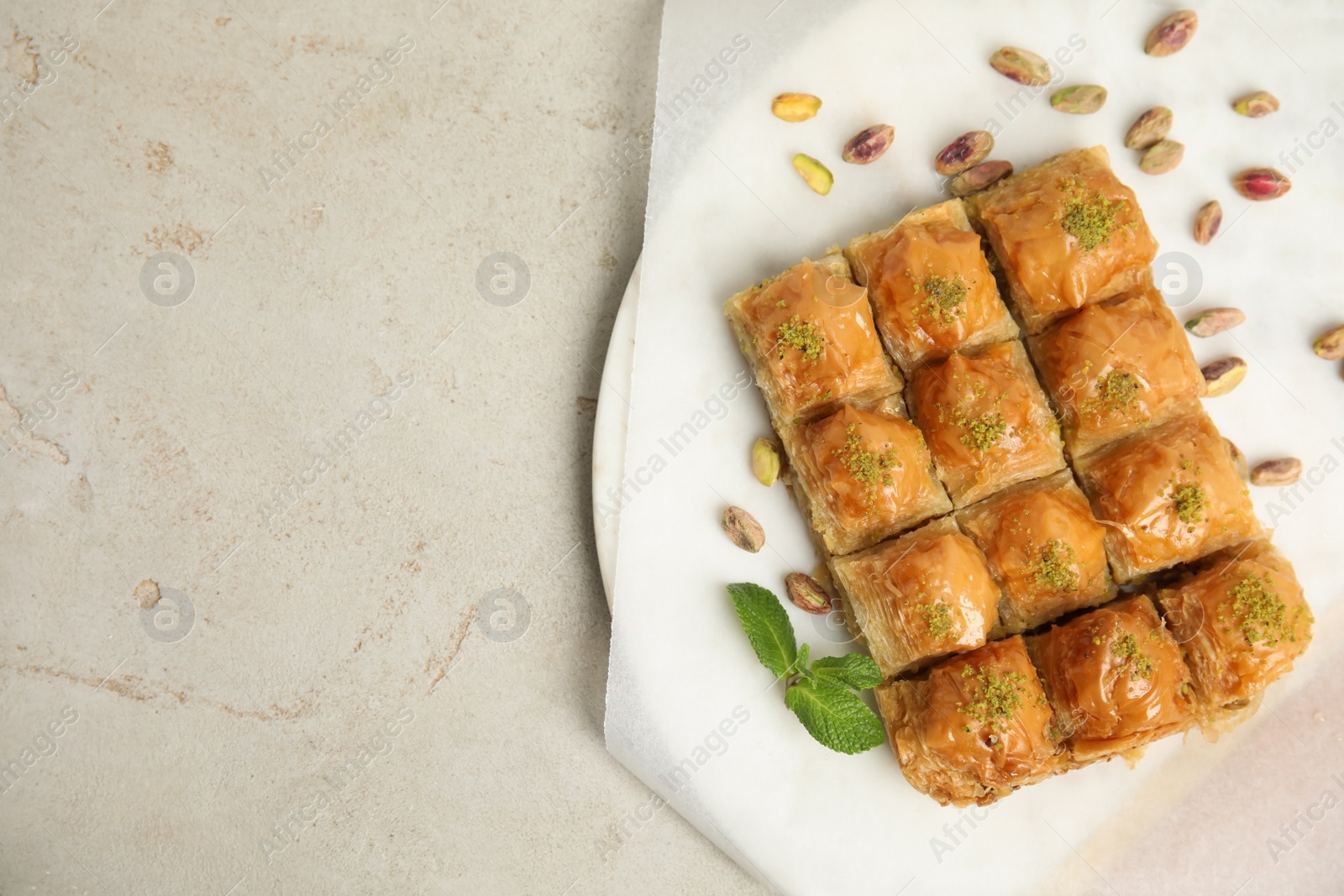 Photo of Delicious sweet baklava with pistachios and mint on light grey table, top view. Space for text