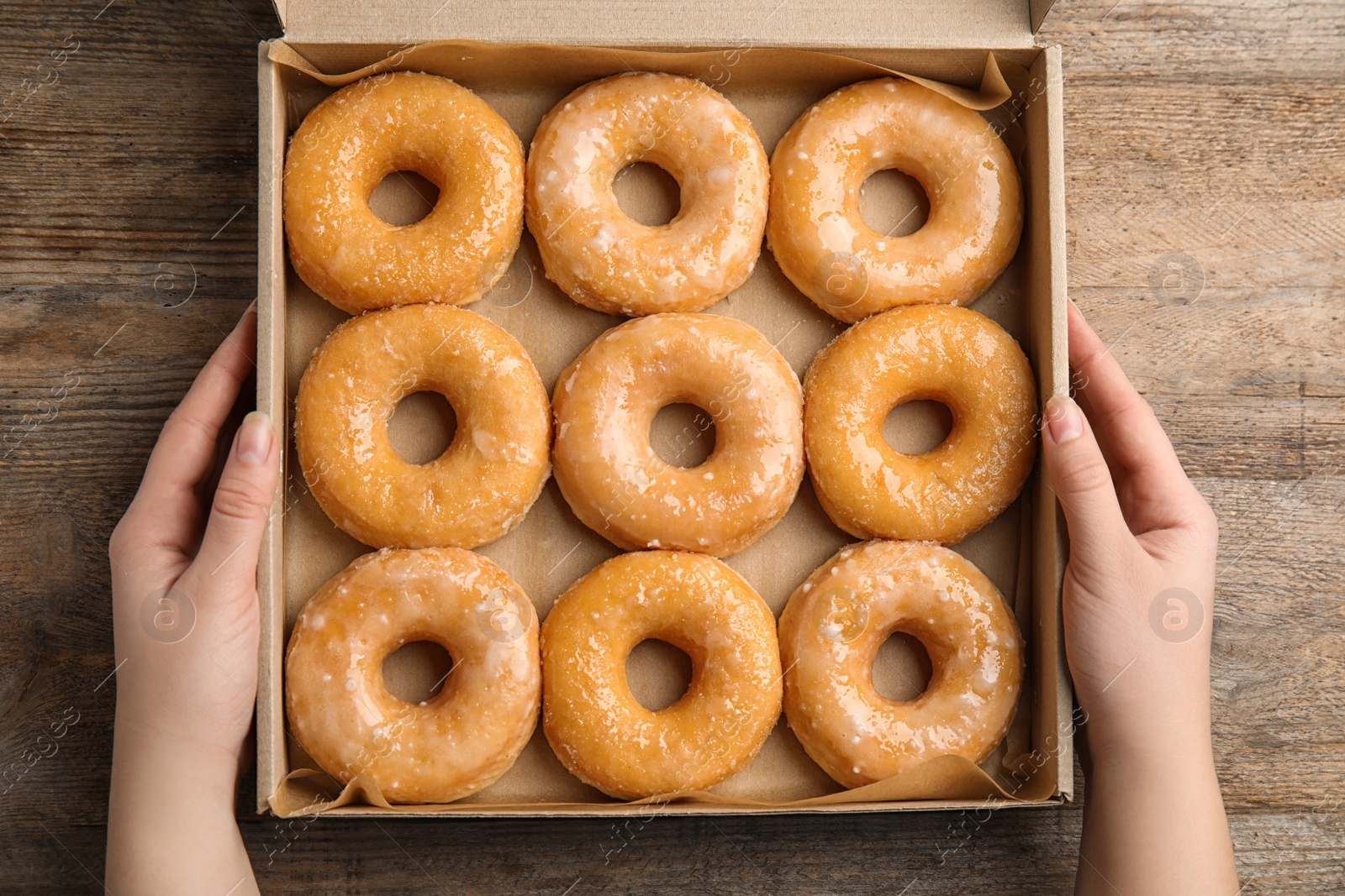 Photo of Woman with box of delicious donuts at wooden table, top view