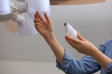 Photo of Woman changing fluorescent light bulb in ceiling lamp at home, closeup. Saving energy concept