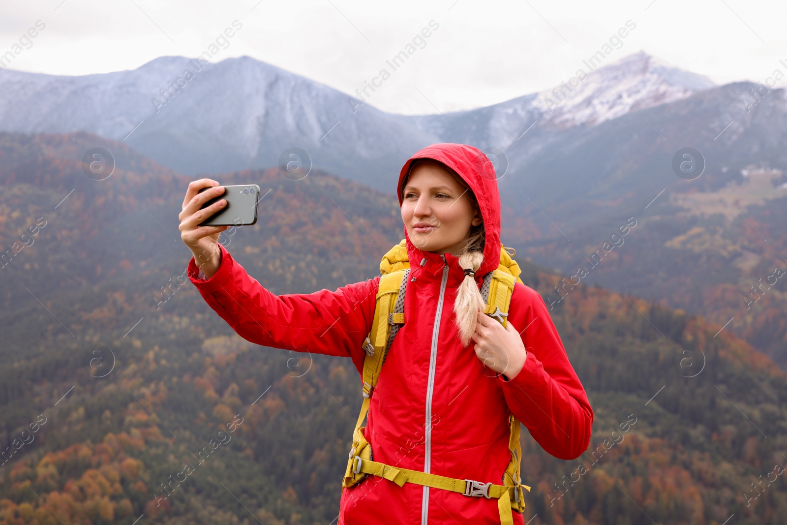 Photo of Happy young woman taking selfie with phone in mountains