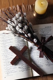 Photo of Cross, Bible, burning candle and willow branches on wooden table, flat lay