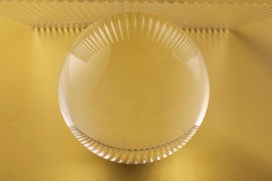 Photo of Transparent glass ball on yellow background, closeup