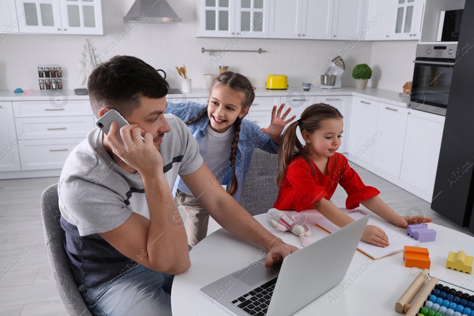 Photo of Children disturbing stressed man in kitchen. Working from home during quarantine