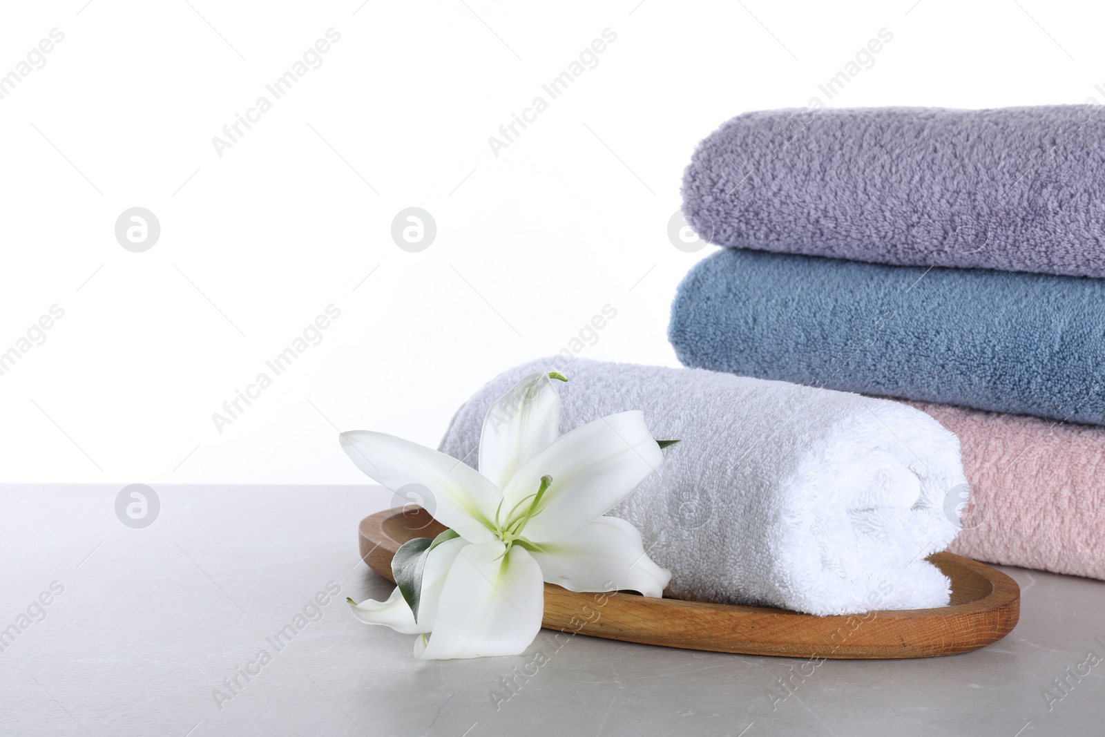 Photo of Fresh towels and lily flower on light grey table against white background
