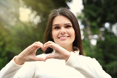Photo of Happy young woman making heart shape with hands outdoors
