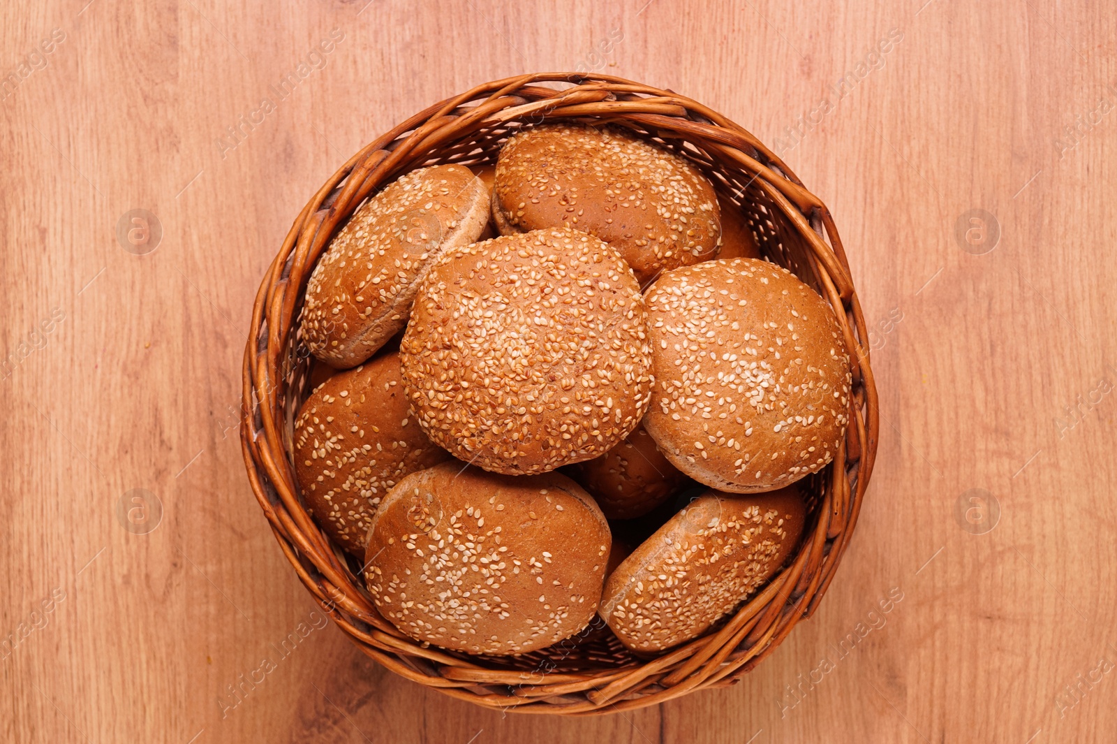 Photo of Wicker basket of fresh buns with sesame seeds on wooden table, top view