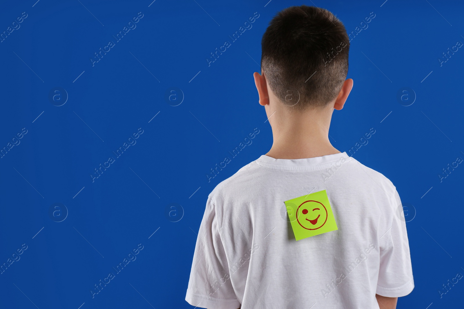 Photo of Preteen boy with winking face sticker on back against blue background, space for text. April fool's day