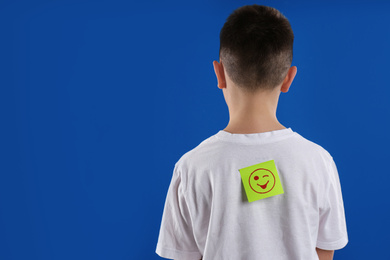 Photo of Preteen boy with winking face sticker on back against blue background, space for text. April fool's day