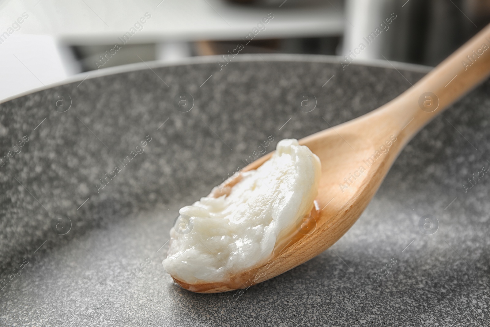 Photo of Wooden spoon with coconut oil in frying pan, closeup. Healthy cooking