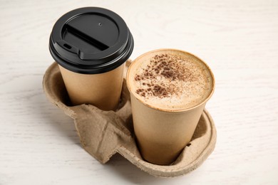 Takeaway paper cups with coffee in cardboard holder on white wooden table