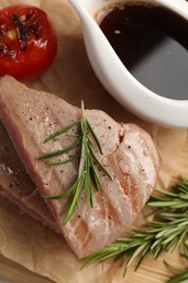 Photo of Pieces of delicious tuna with rosemary, tomato and sauce on board, top view