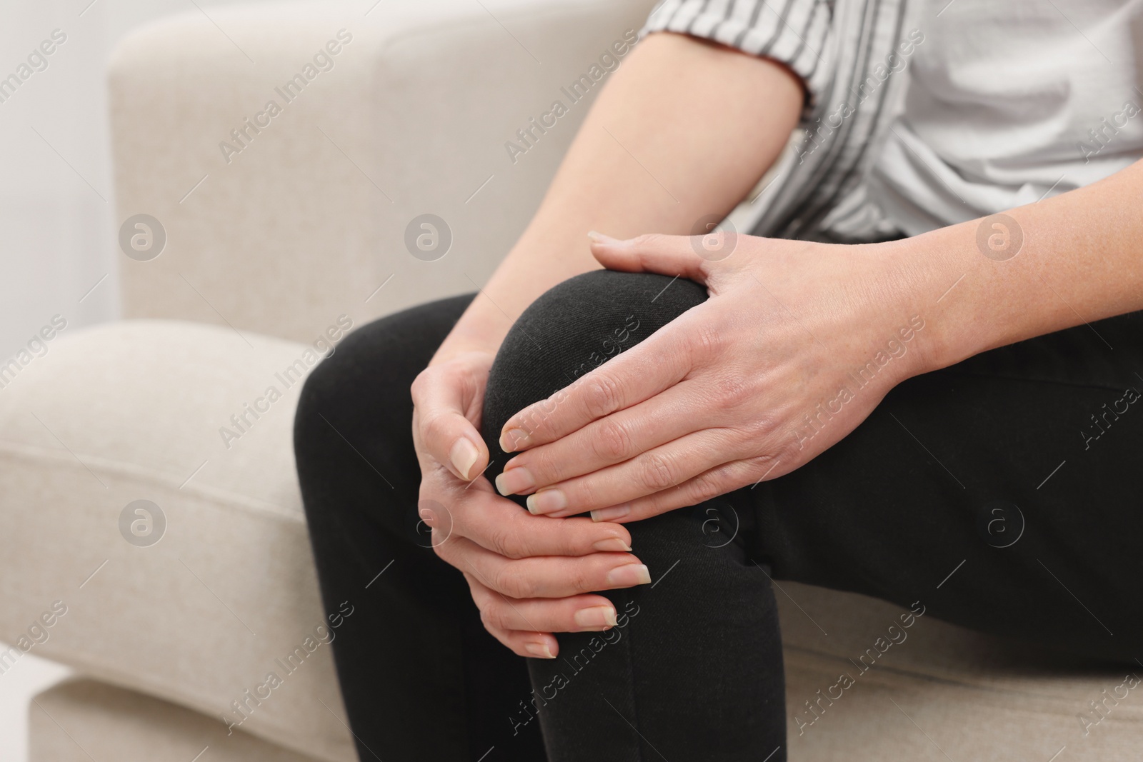 Photo of Woman suffering from knee pain on sofa indoors, closeup. Arthritis symptoms