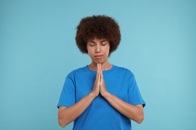 Photo of Woman with clasped hands praying to God on light blue background