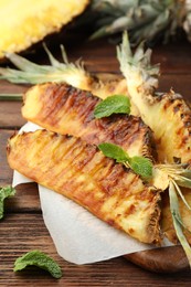 Photo of Tasty grilled pineapple pieces and mint leaves on wooden table, closeup