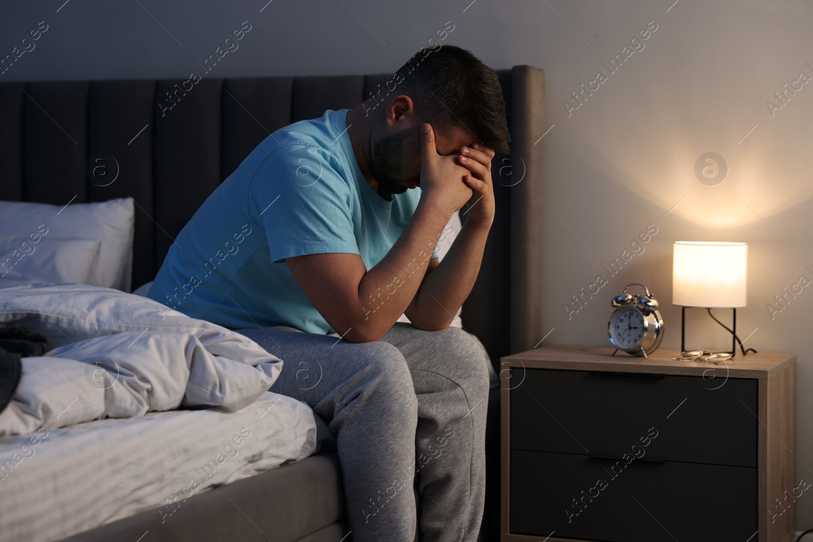 Photo of Man covering face with hands on bed indoors