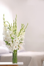 Photo of Vase with beautiful white gladiolus flowers on wooden table in bedroom