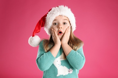 Cute child in Santa hat on pink background. Christmas celebration