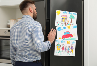 Man opening refrigerator door with child's drawings in kitchen