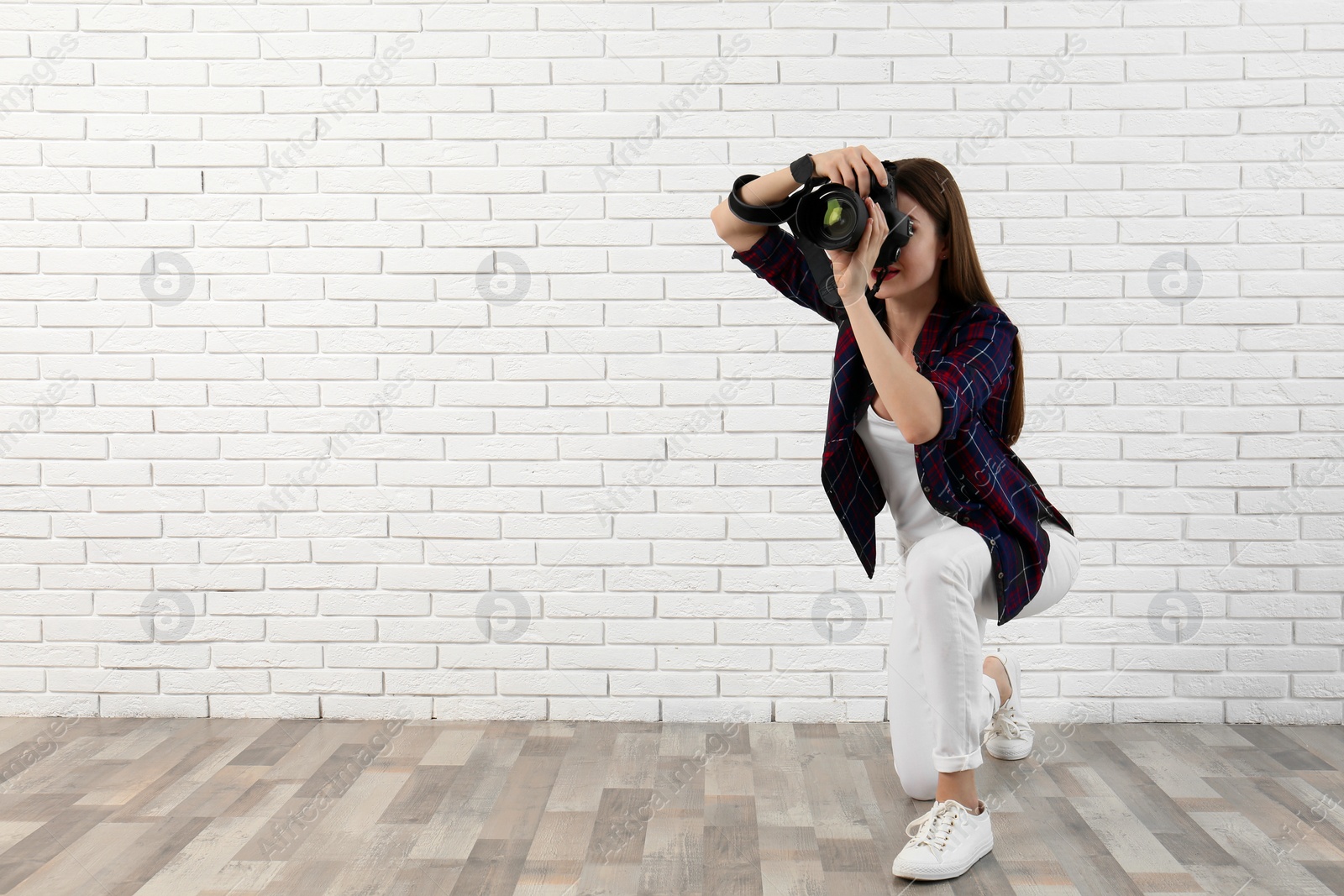 Photo of Professional photographer taking picture near white brick wall. Space for text