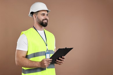 Photo of Engineer in hard hat holding clipboard on brown background, space for text