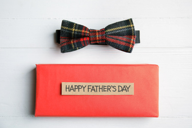 Photo of Bow tie and gift box with words HAPPY FATHER'S DAY on white wooden background, flat lay