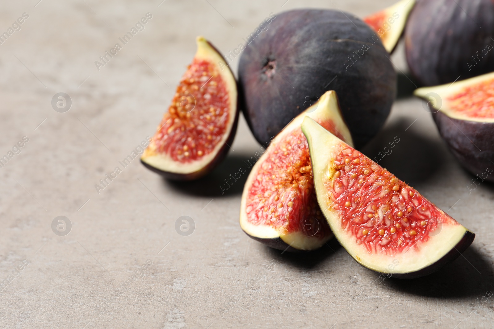 Photo of Whole and cut ripe figs on light grey textured table, closeup. Space for text