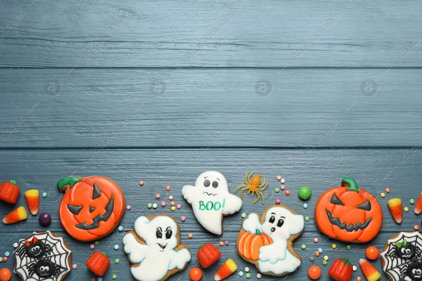 Photo of Tasty cookies and sweets for Halloween party on blue wooden table, flat lay. Space for text