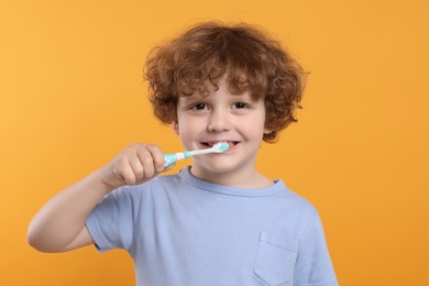 Photo of Cute little boy brushing his teeth with plastic toothbrush on yellow background