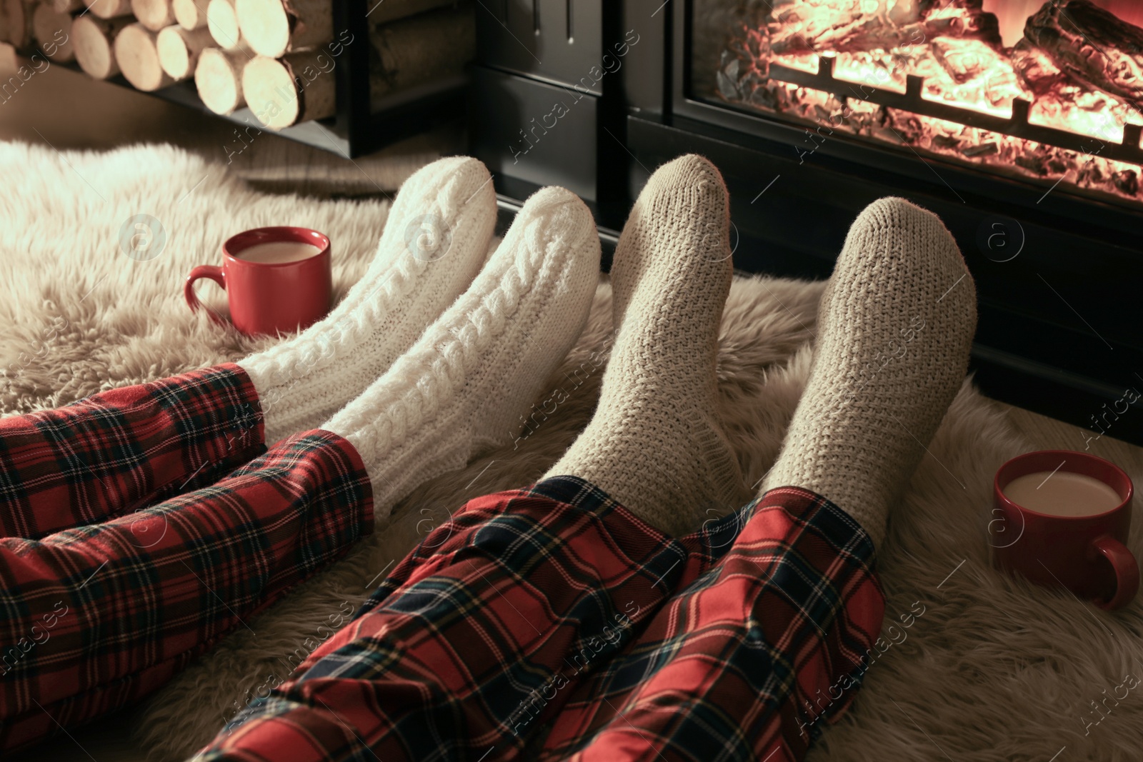 Photo of Couple in knitted socks near fireplace at home, closeup of legs