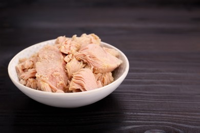 Bowl with canned tuna on black wooden table, closeup. Space for text
