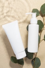 Eucalyptus leaves and face cleansing products in water against beige background, flat lay