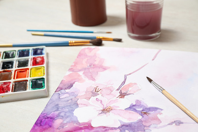 Photo of Beautiful floral picture, brushes and watercolor paints on light table, closeup