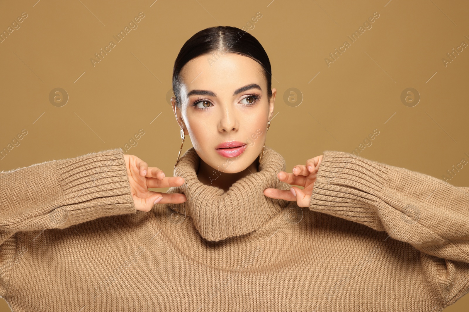 Photo of Beautiful young woman with elegant earrings on light brown background