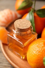 Photo of Bottle of tangerine essential oil and fresh fruits on wooden table, closeup