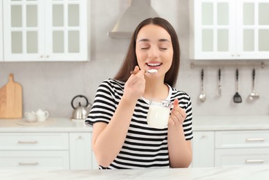 Happy woman eating tasty yogurt in kitchen