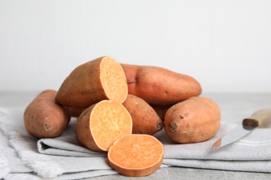 Photo of Whole and cut ripe sweet potatoes on grey table