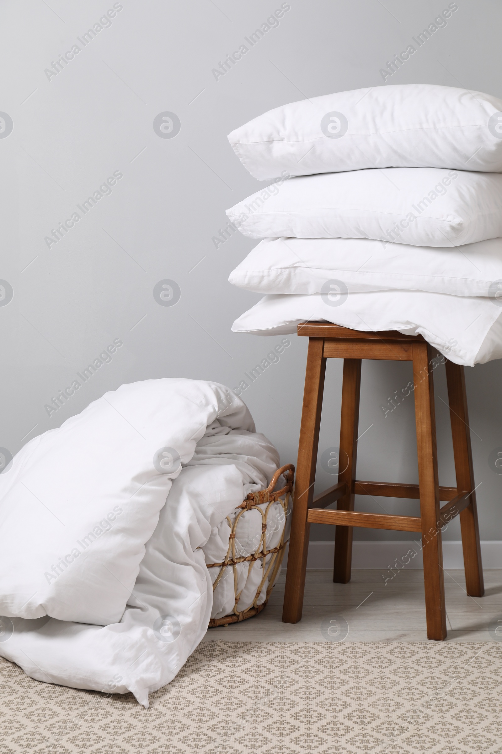 Photo of Soft pillows, duvet and chair near light grey wall indoors