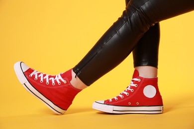 Photo of Woman wearing pairnew stylish sneakers on yellow background, closeup