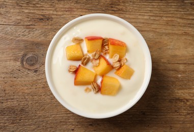 Photo of Tasty peach yogurt with granola and pieces of fruit in bowl on wooden table, top view