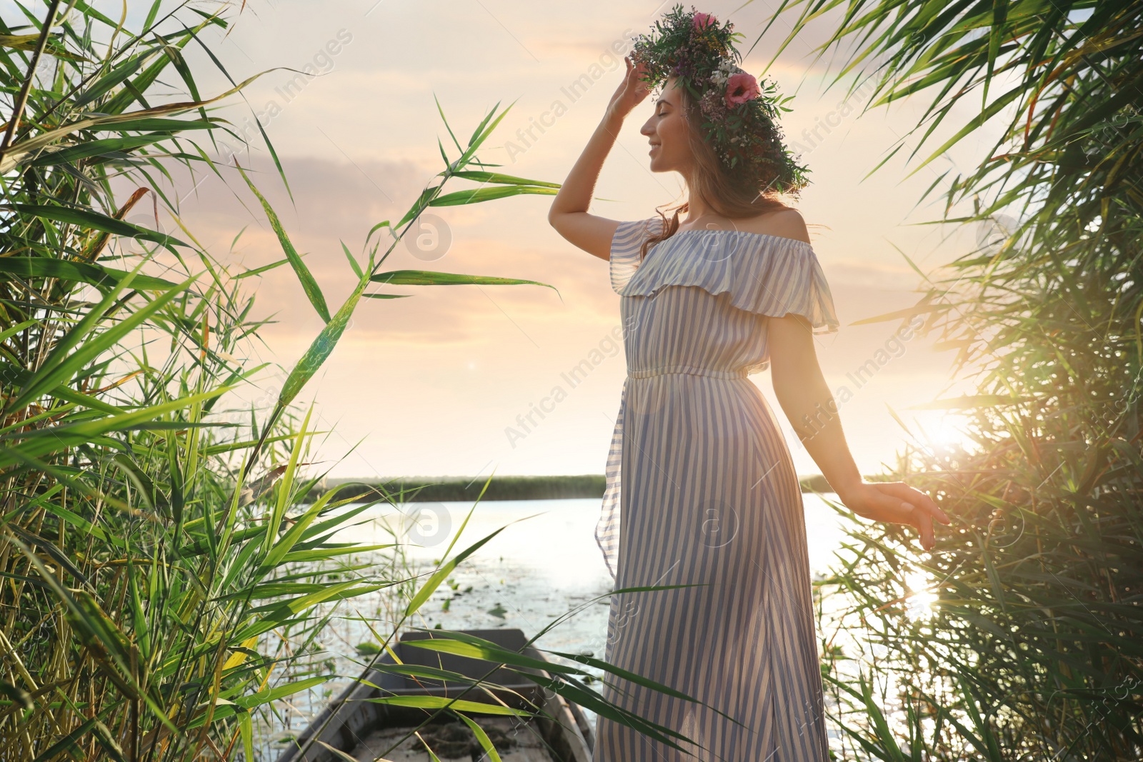 Photo of Young woman wearing wreath made of beautiful flowers near river on sunny day