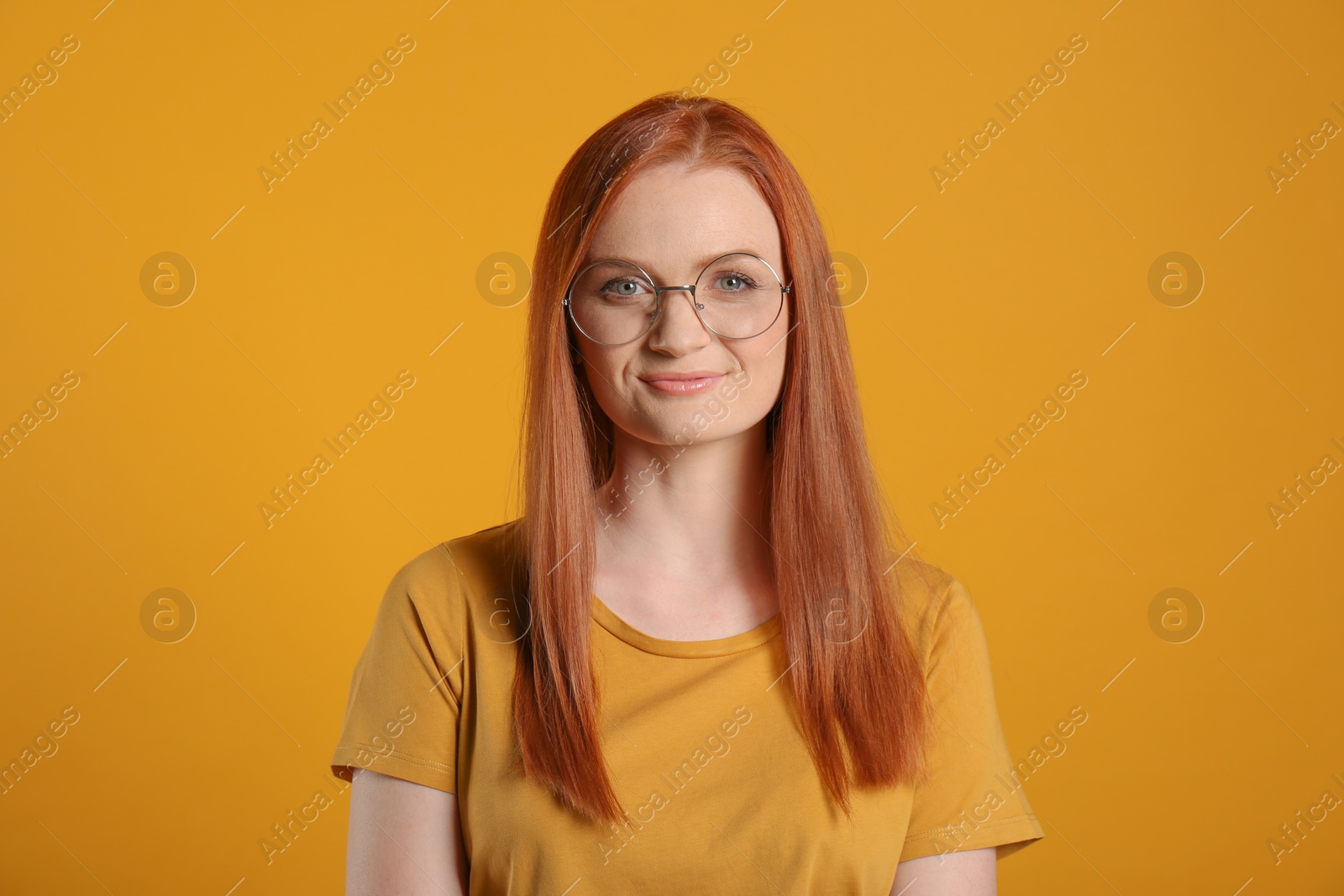 Photo of Candid portrait of happy young woman with charming smile and gorgeous red hair on yellow background