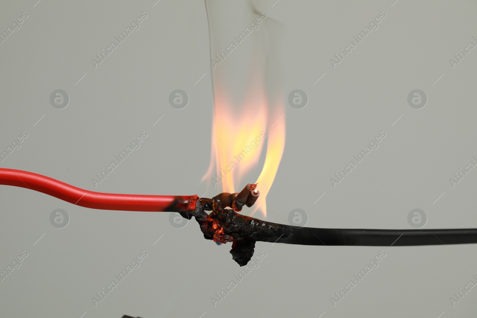 Photo of Inflamed red wire on grey background, closeup. Electrical short circuit