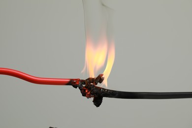 Inflamed red wire on grey background, closeup. Electrical short circuit