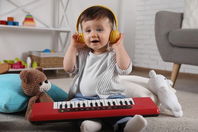Photo of Cute little boy in headphones with toy piano at home