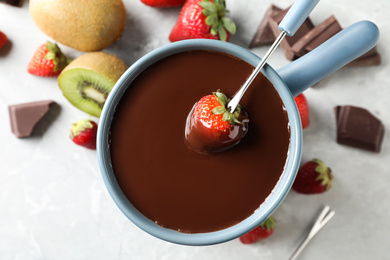 Photo of Dipping strawberry into fondue pot with chocolate on light table, top view