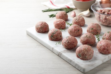 Many fresh raw meatballs on white wooden table, space for text