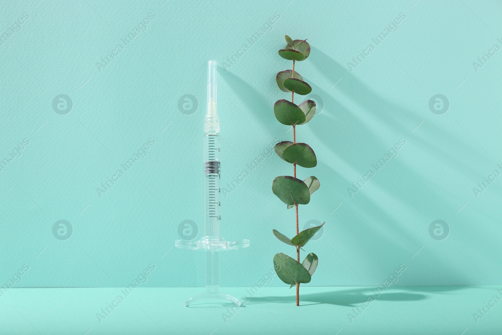 Photo of Cosmetology. Medical syringe and eucalyptus branch on turquoise background