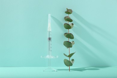Photo of Cosmetology. Medical syringe and eucalyptus branch on turquoise background