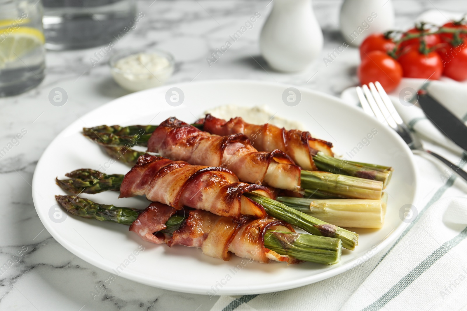 Photo of Oven baked asparagus wrapped with bacon on white marble table